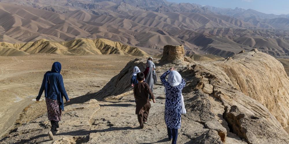 In a barren mountainous landscape in Afghanistan, four girls and a boy walk along a ridge.